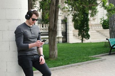 Young man listening music on mobile phone while standing by column