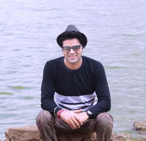 Portrait of happy man wearing hat while sitting on rock by lake