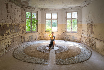 Portrait of young man holding illuminated lighting equipment while kneeling in abandoned house