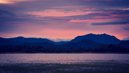 Scenic view of lake by silhouette mountains against romantic sky