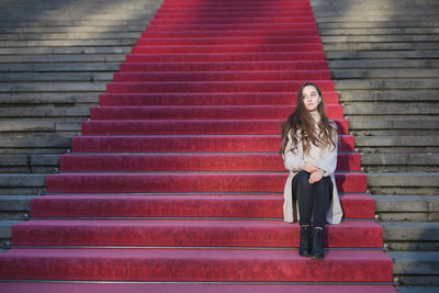 Full length of woman looking away while sitting on red staircase