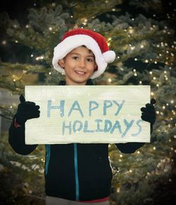 Portrait of boy holding text on paper against christmas tree