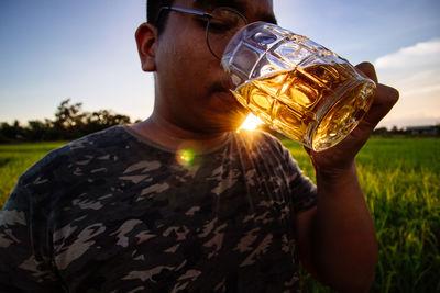 Midsection of man drinking glass on field against sky