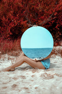 Rear view of woman sitting on sand at beach with a big mirror