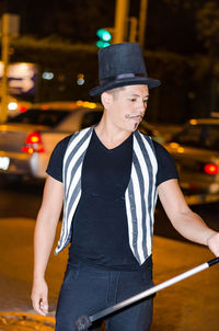 Man wearing hat while holding rode on street in city at night