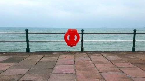 Red railing by sea against sky