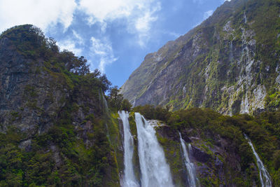 Low angle view of waterfall amidst rocks against sky