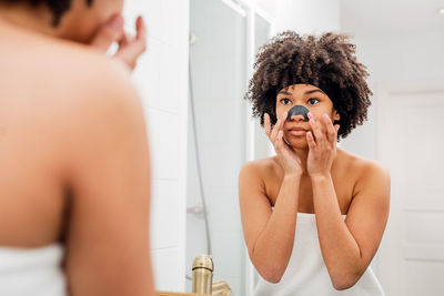 Reflection of woman applying facial mask in mirror at home