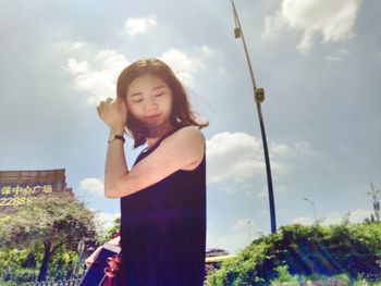 Low angle view of young woman standing against cloudy sky