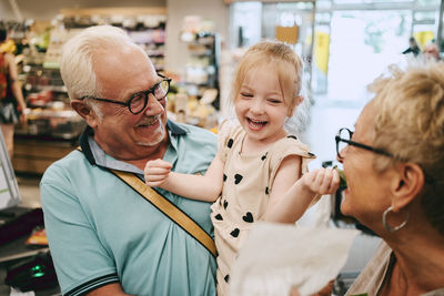 Cheerful girl having fun with grandmother while shopping at supermarket