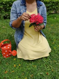 Midsection of woman holding red flower on field