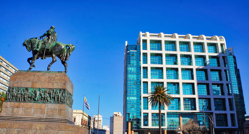 Low angle view of statue against building against clear blue sky