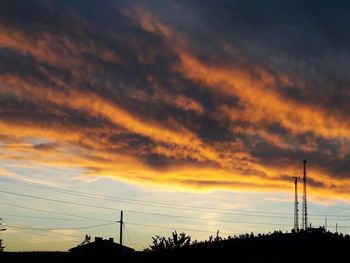 Low angle view of silhouette electricity pylon against sky during sunset