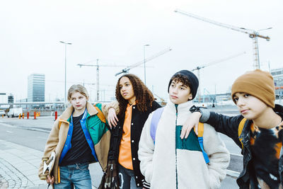 Girls and boys looking away while standing on street against clear sky