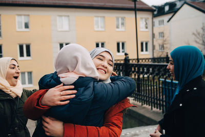 Happy muslim women embracing by friends in city