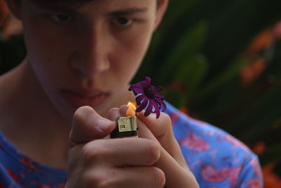 Teenage boy burning purple flower through cigarette lighter