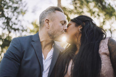 Back lit mature groom kissing young bride during wedding