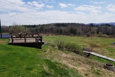 Empty bench on field by trees against sky