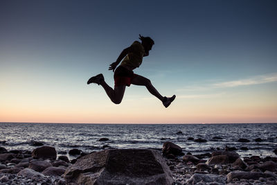 Man jumping at beach against sky during sunset
