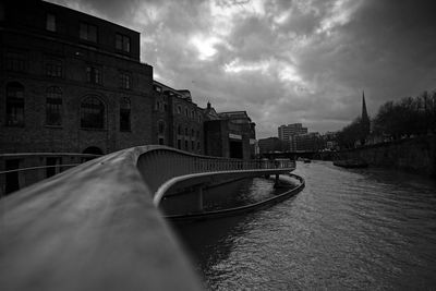 Bridge over river by buildings in city against sky