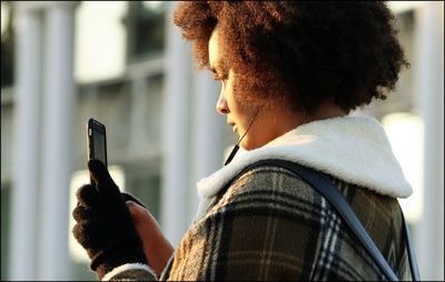 Side view of young woman holding mobile phone