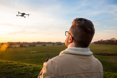 Man flying drone over field against sky during sunset