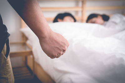 Cropped hand clenching fist against couple sleeping on bed