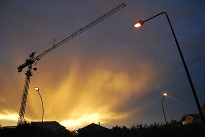 Low angle view of crane and street lights against sky during sunset