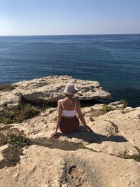 Rear view of woman sitting on shore by sea against sky