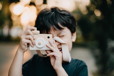 Close-up of happy boy photographing with toy camera at park during sunset