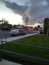 Cars on road by buildings against sky during sunset