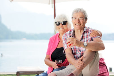 Portrait of senior couple sitting against lake