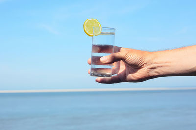 Close-up of hand holding glass of water against blue sky