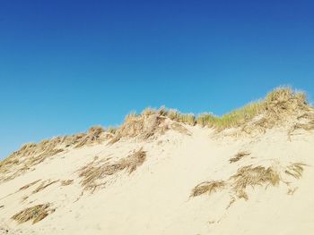 Low angle view of sand dune against clear blue sky