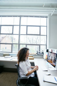 Smiling businesswoman video conferencing with colleagues over desktop computer in office