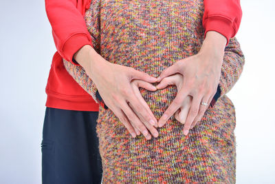 Midsection of man with woman making heart shaped on stomach against white background