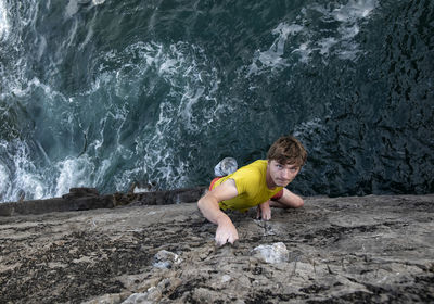 Passionate young male rock climber climbing rocky cliff by sea