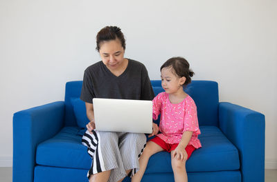 Full length of mother and daughter sitting on sofa