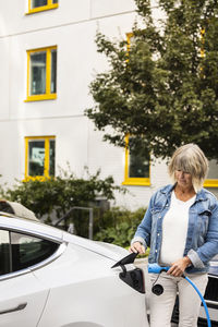 Senior woman charging electric car outdoors