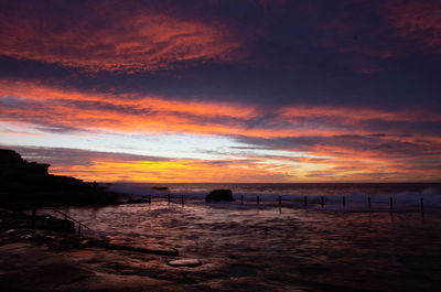 Scenic view of beach against dramatic sky during sunset