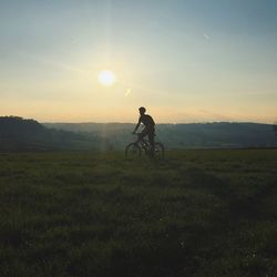 Man cycling on field against sky during sunset