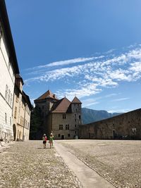 Rear view of people walking on building against blue sky