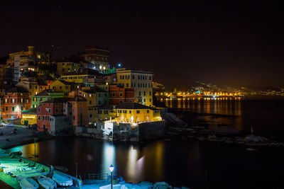 Illuminated buildings by river against sky at night