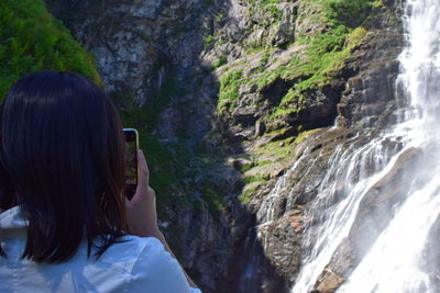 Rear view of woman photographing waterfall