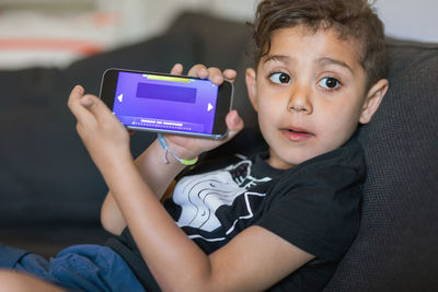 Boy showing game displayed on smart phone screen at home