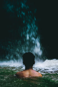 Rear view of shirtless woman standing in water