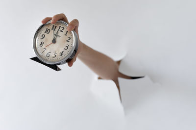 Close-up of hand holding clock over white background