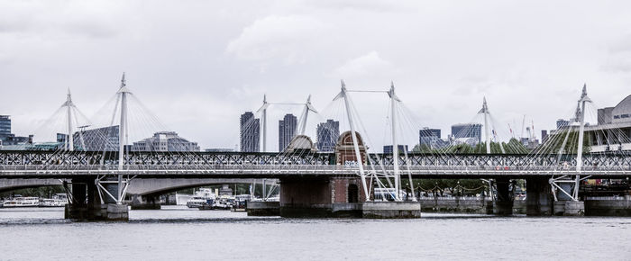 Bridge over river in city against cloudy sky