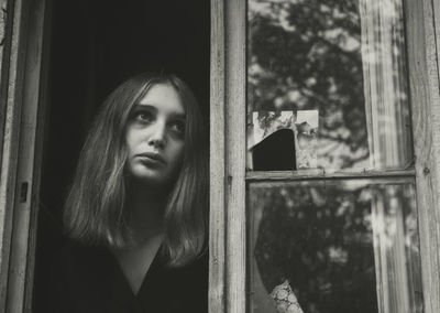 Portrait of young woman looking through window