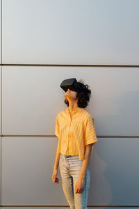 Young woman wearing virtual reality headset in front of wall
